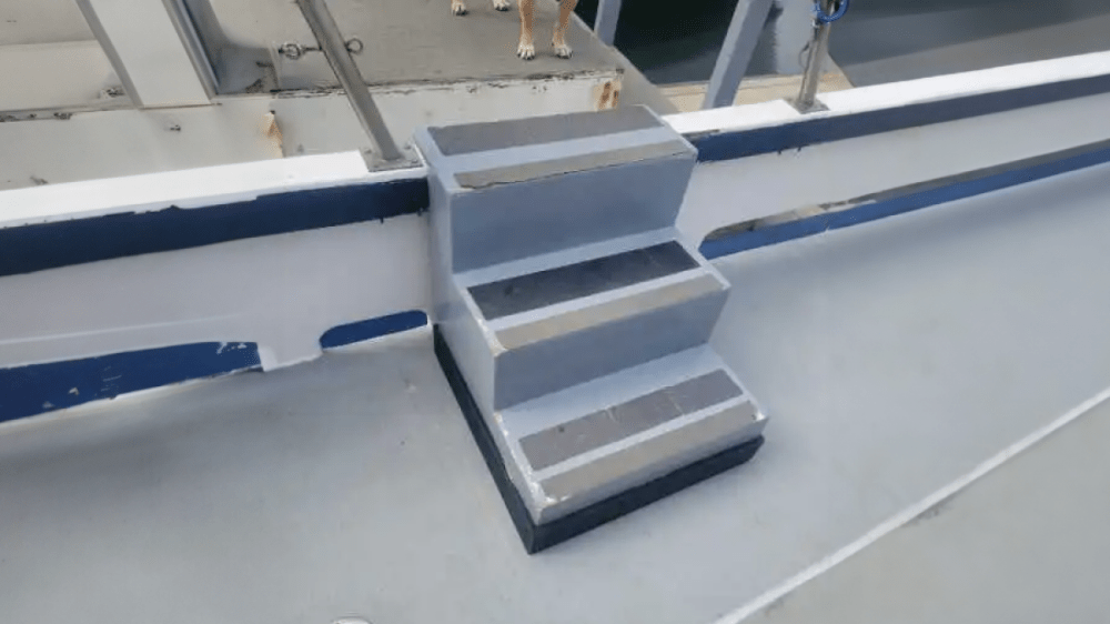 Small metal steps on a boat deck leading to a dock with railings.