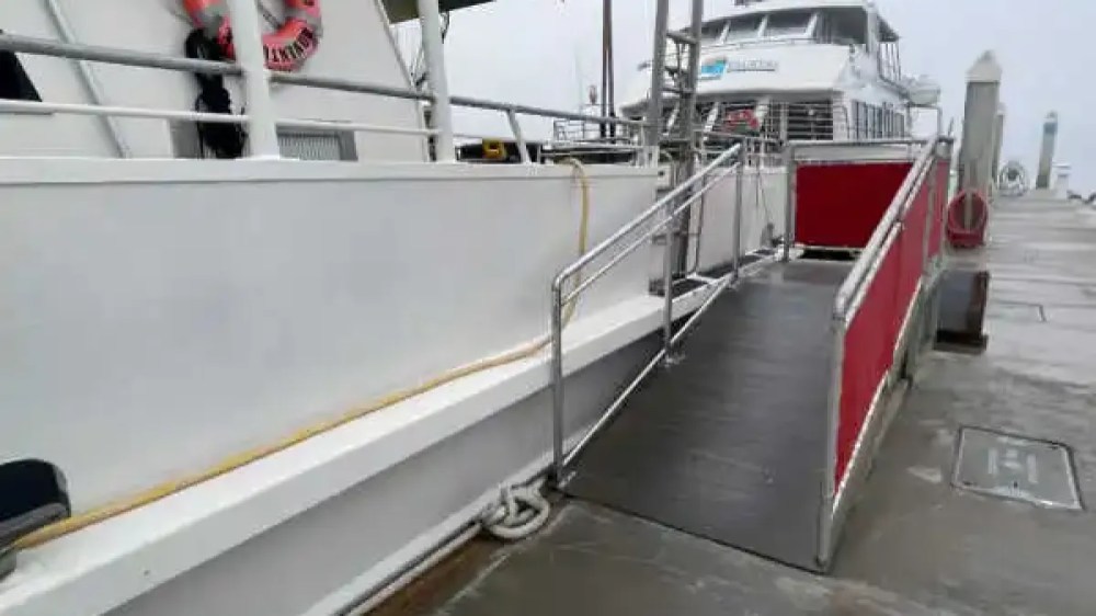 A boat docked with a ramp leading onto it, next to a pier on a cloudy day.