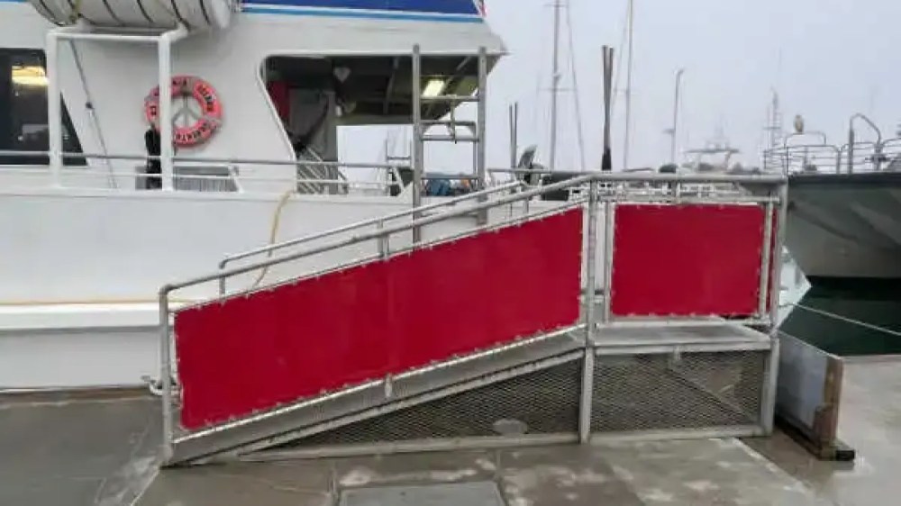 Metal ramp with red paneling leading to a boat on a dock.