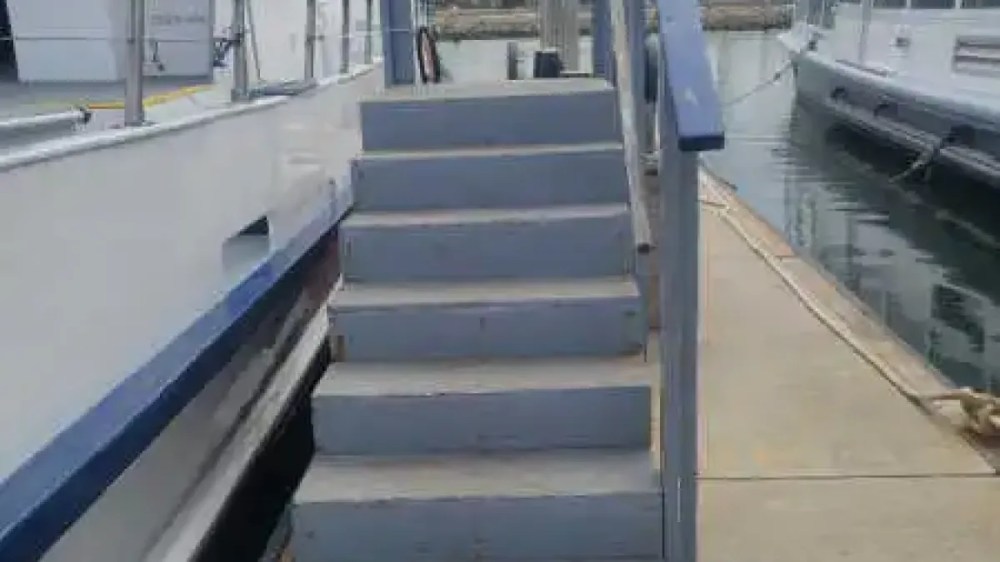 Wooden stairs with rails leading from a dock to a boat on calm water.