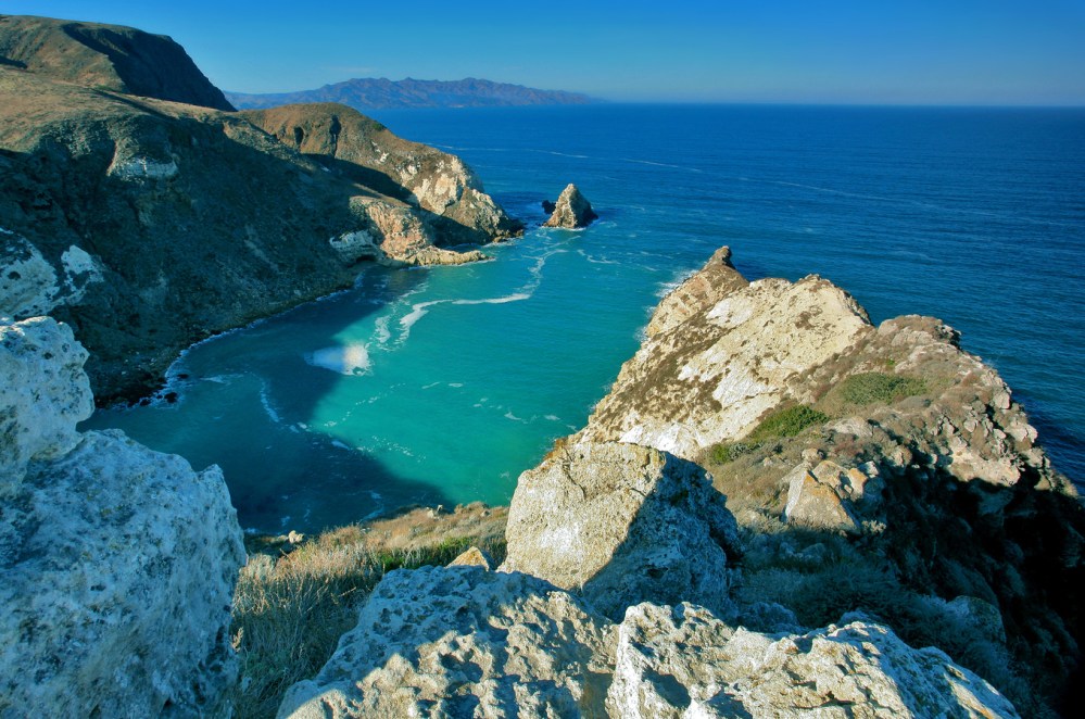 a rocky cliff with water and a mountain in the background