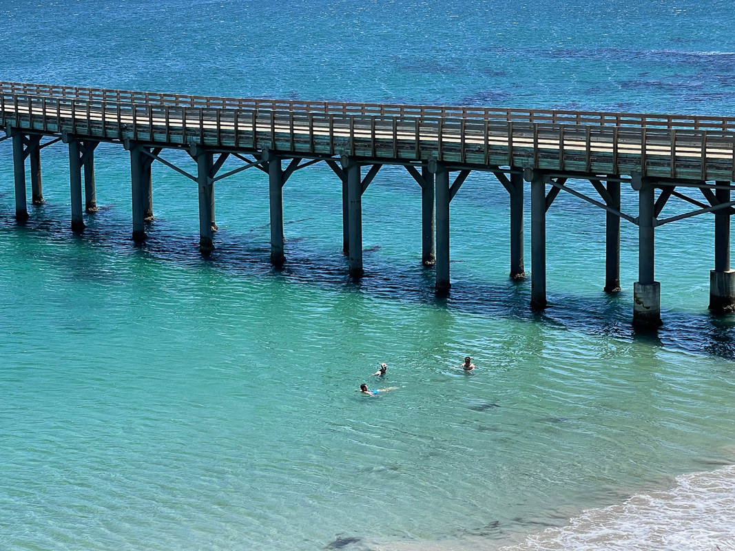 a group of people on a pier next to a body of water with Royal Border Bridge in the background
