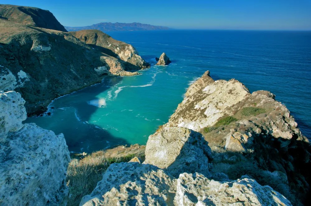 a rocky cliff with water and a mountain in the background